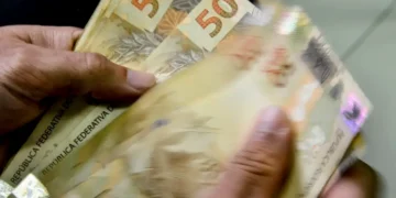 Notas de 50 reais sendo contadas, simbolizando o salário mínimo de 2026.