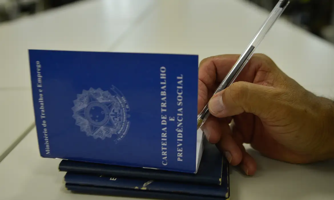 Pilha de carteiras de trabalho físicas azuis sobre uma mesa branca, com uma caneta preta à direita.