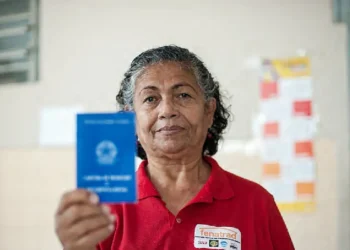 Mulher de meia-idade sorrindo e segurando uma carteira de trabalho azul em ambiente interno