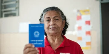Mulher de meia-idade sorrindo e segurando uma carteira de trabalho azul em ambiente interno