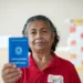 Mulher de meia-idade sorrindo e segurando uma carteira de trabalho azul em ambiente interno