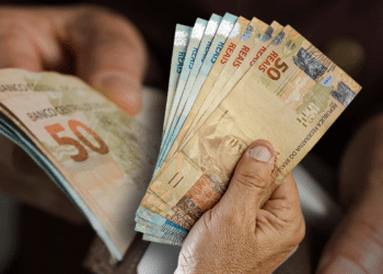 Notas de R$50 e R$100 sendo seguradas, representando o valor do PIS/PASEP de 2026 com o aumento do salário mínimo.