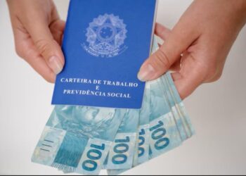 Carteira de Trabalho e Previdência Social com cédulas de 100 reais, simbolizando a atualização do salário mínimo e seus impactos no Seguro-Desemprego em 2026.