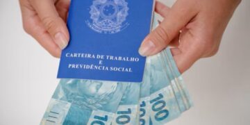 Carteira de Trabalho e Previdência Social com cédulas de 100 reais, simbolizando a atualização do salário mínimo e seus impactos no Seguro-Desemprego em 2026.
