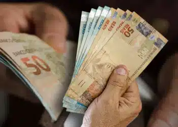 Mãos de pessoa idosa segurando e contando notas de cinquenta reais