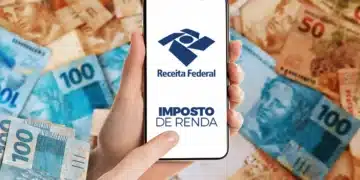 Mão segura celular com tela da Receita Federal sobre diversas notas de real