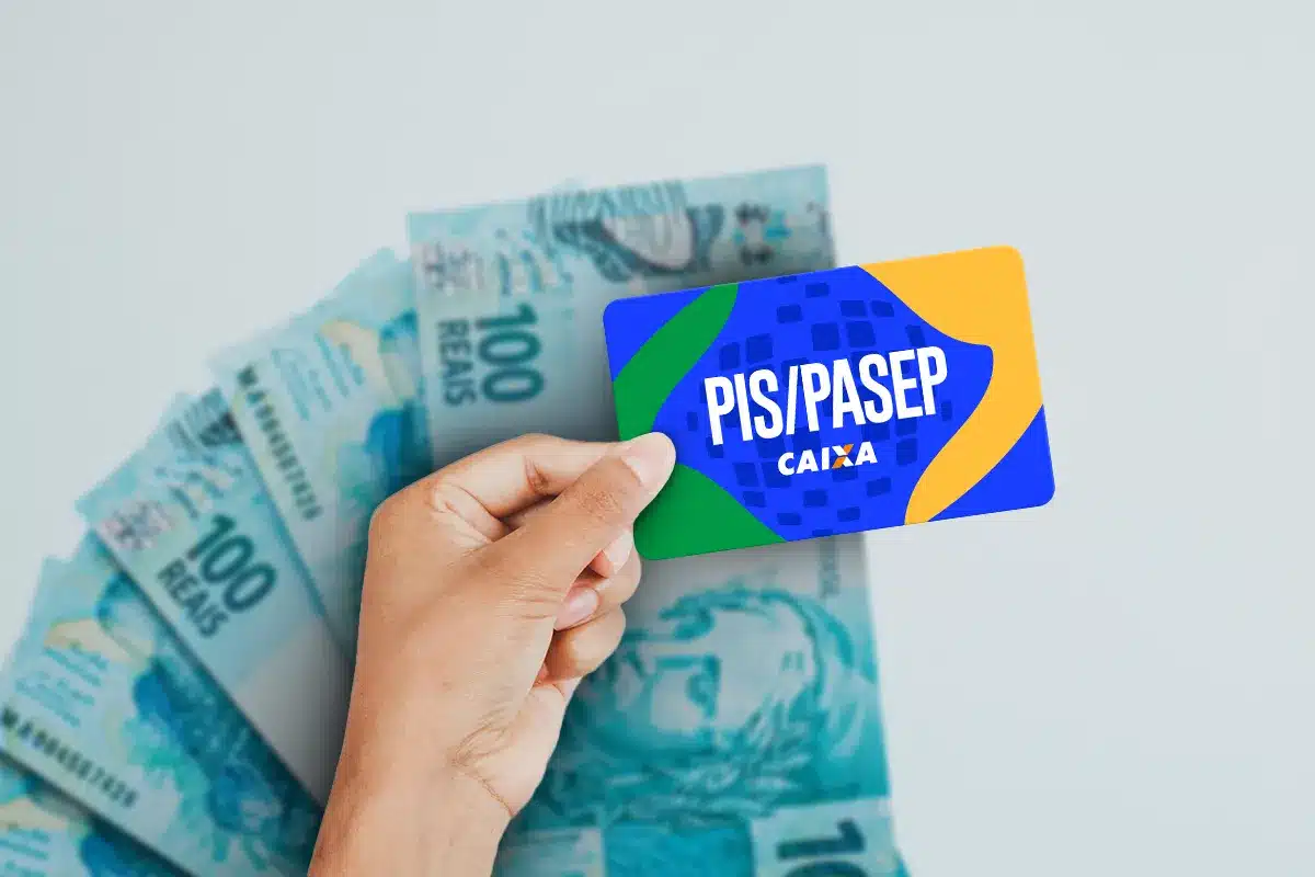 Cartão PIS/PASEP Caixa e notas de cem reais em destaque Mão segura cartão PIS/PASEP Caixa com notas de R$ 100 ao fundo