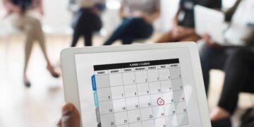 Pessoa aponta para data circulada em calendário digital durante reunião de equipe