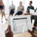 Pessoa aponta para data circulada em calendário digital durante reunião de equipe