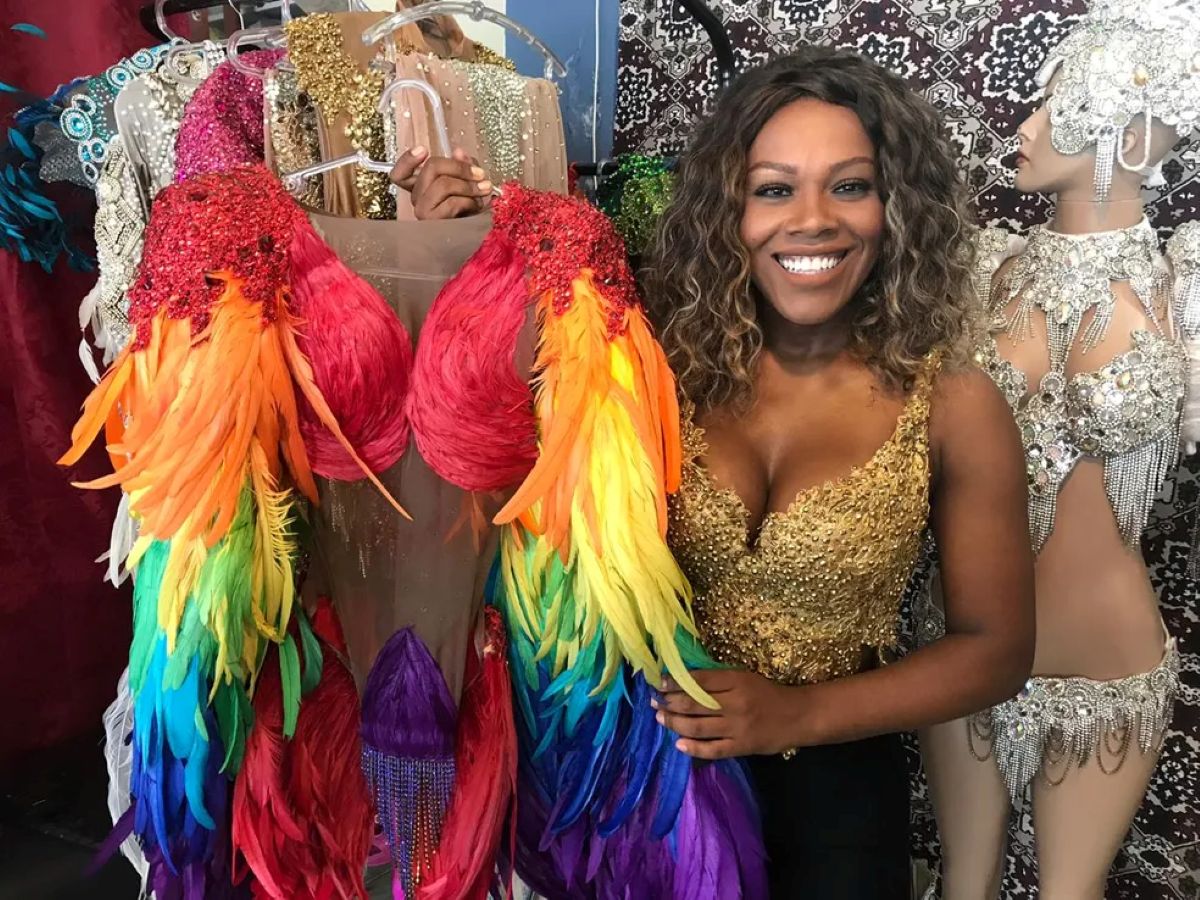 Empreendedora ao lado de fantasias carnavalescas coloridas e decoradas em ateliê, mostrando exemplo de negócio lucrativo no Carnaval 2026.