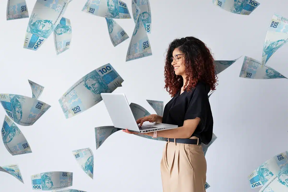 Como consultar se há valores em seu nome e resgatar dinheiro esquecido em 2026 Mulher usando notebook cercada por notas de dinheiro simbolizando consulta de valores esquecidos em seu nome em 2026