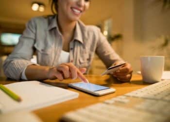 Mulher sorrindo consulta saldo em smartphone com cartão em mãos