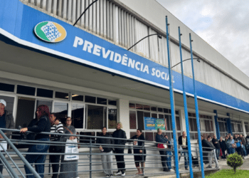 Fila de segurados em frente a agência do INSS aguardando atendimento presencial durante mutirão com vagas limitadas em 2026.