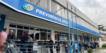 Fila de segurados em frente a agência do INSS aguardando atendimento presencial durante mutirão com vagas limitadas em 2026.