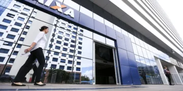 Mulher caminha em frente à entrada de agência da Caixa com prédio espelhado ao fundo