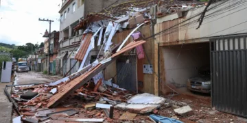 Casa destruída com telhado desabado e escombros espalhados pela rua após enchentes na Zona da Mata mineira; Caixa libera saque de até R$ 6.220 do FGTS para moradores afetados.