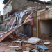 Casa destruída com telhado desabado e escombros espalhados pela rua após enchentes na Zona da Mata mineira; Caixa libera saque de até R$ 6.220 do FGTS para moradores afetados.
