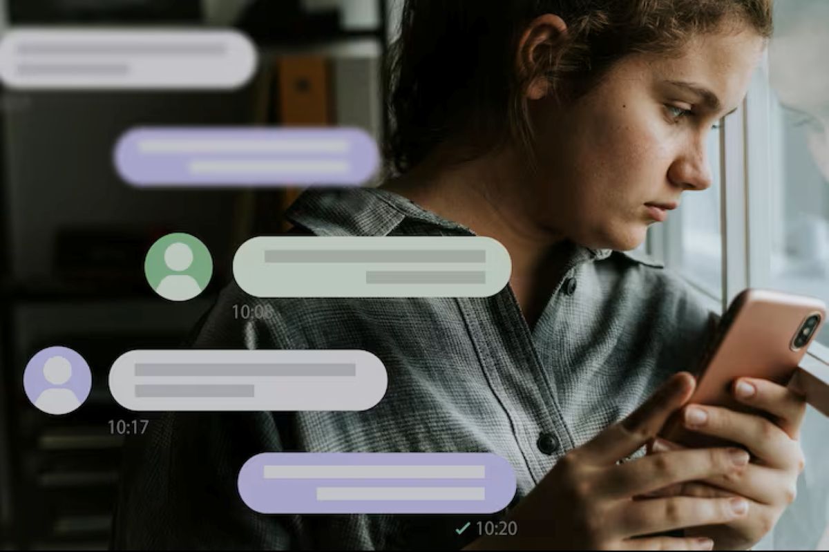 Usuária olha o celular com dúvidas sobre possível bloqueio no WhatsApp enquanto mensagens aparecem desfocadas ao fundo