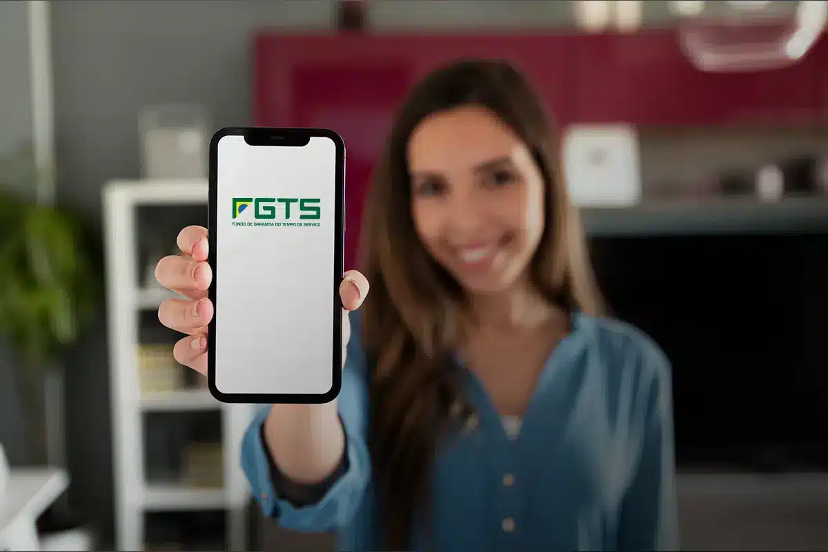 Aplicativo do FGTS. Mulher sorrindo ao segurar seu celular na tela inicial do aplicativo do FGTS.