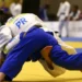 Dois atletas de judô competem no tatame, um aplicando golpe de queda com uniforme azul.
