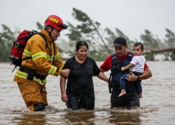Bombeiro e voluntário resgatam mulher e criança em água barrenta de enchente.