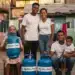 Grupo familiar sorrindo com botijões do Gás do Povo em área residencial simples