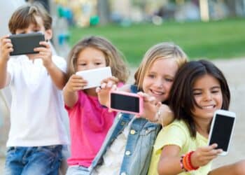 Grupo de crianças sorrindo enquanto tiram selfies com celulares ao ar livre.
