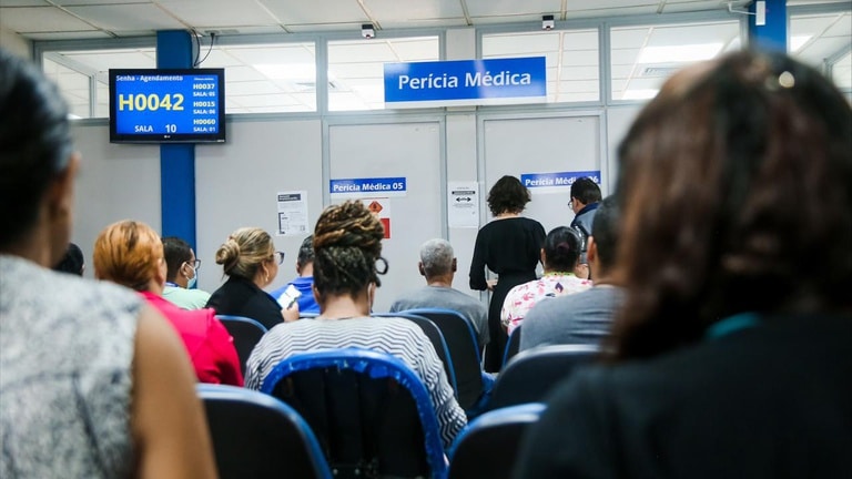 Segurados aguardando atendimento em sala de espera de agência do INSS com placas de Perícia Médica ao fundo — nova portaria do Atestmed amplia análise documental e pode reduzir necessidade de perícia presencial