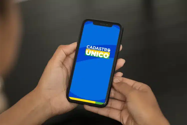 CadÚnico: desconto conta de luz Pessoa segura celular exibindo a tela azul do aplicativo Cadastro Único