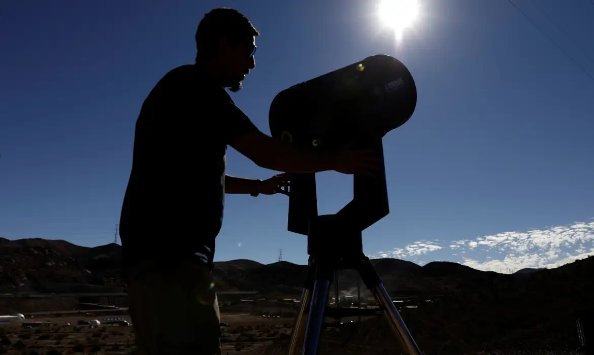 Eclipse Solar 2027 — Astrônomo Observa o Sol com Telescópio Silhueta de pessoa com telescópio apontado para o Sol em céu aberto, ilustrando a observação do eclipse solar total de 2027, o mais longo do século XXI.