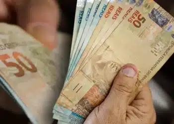 Mão segurando cédulas de cinquenta reais em contagem detalhada