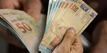 Mão segurando cédulas de cinquenta reais em contagem detalhada
