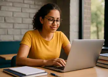 Jovem digitando em notebook com livros e caderno sobre a mesa