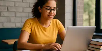 Jovem digitando em notebook com livros e caderno sobre a mesa