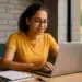 Jovem digitando em notebook com livros e caderno sobre a mesa