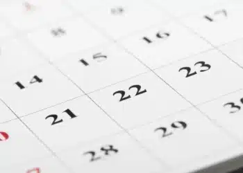 Calendário de parede com datas em preto e vermelho em destaque, com o número 20 em vermelho e o 21 em preto visíveis, representando o ponto facultativo e o feriado de Tiradentes em abril de 2026.