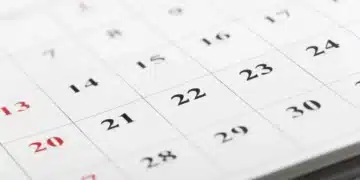 Calendário de parede com datas em preto e vermelho em destaque, com o número 20 em vermelho e o 21 em preto visíveis, representando o ponto facultativo e o feriado de Tiradentes em abril de 2026.