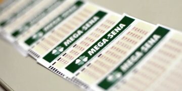 Close detalhado em perspectiva de vários volantes de aposta da Mega-Sena, alinhados sobre uma superfície branca, focando no título "MEGA-SENA" em verde e nos números impressos.