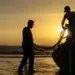 ois trabalhadores puxando rede de pesca na praia com barco ao entardecer
