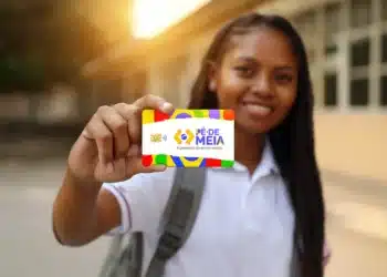 Jovem estudante sorrindo segurando o cartão do programa Pé-de-Meia — A poupança do ensino médio — em frente à escola, representando o recebimento do Incentivo-Matrícula de R$ 200 pago pelo MEC na primeira rodada de pagamentos de 2026, organizada por mês de nascimento