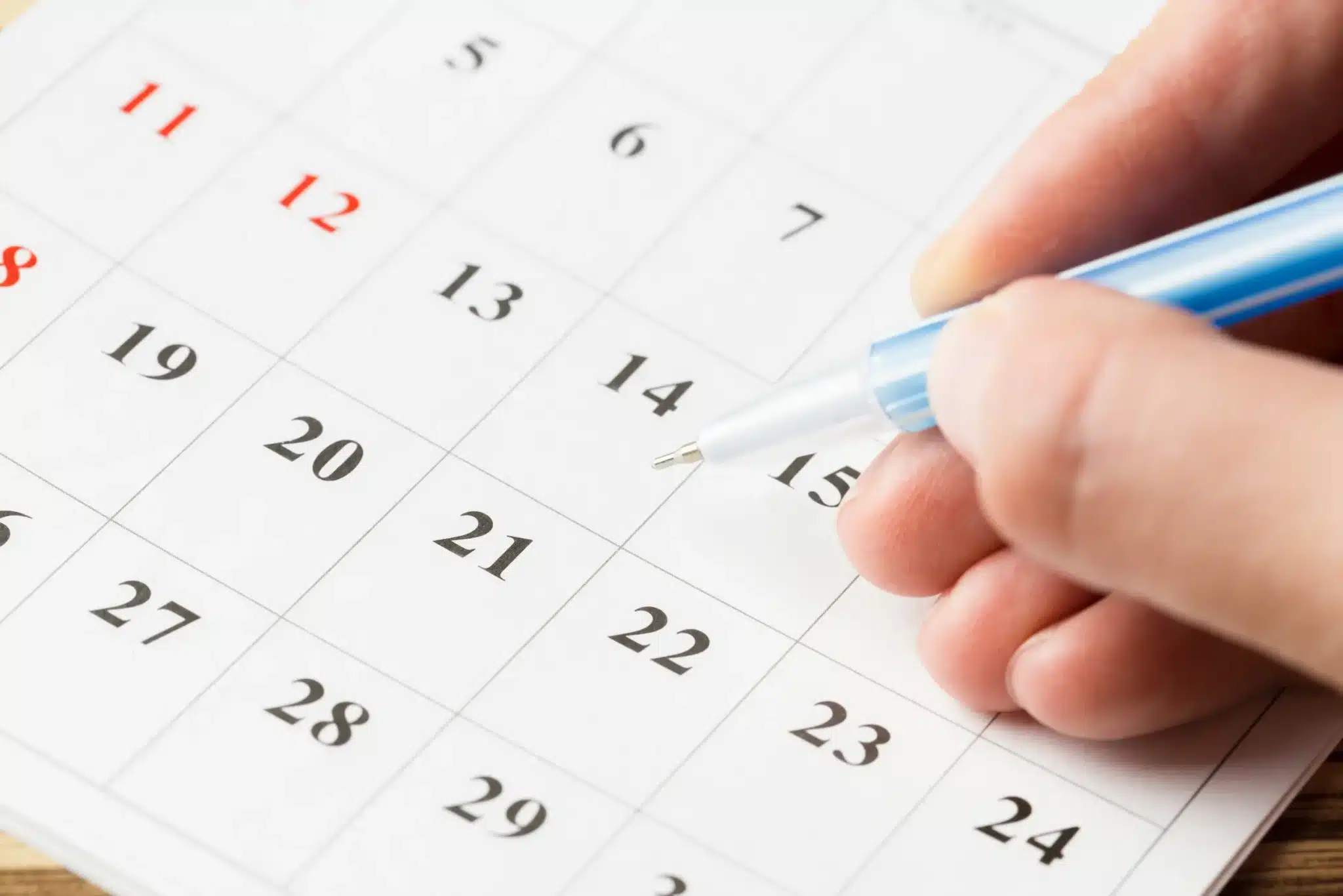 Feriados de abril de 2026: calendário com Paixão de Cristo (03/04) e Tiradentes (21/04) Mão segurando caneta azul apontando para o calendário com as datas 20 e 21 de abril marcadas, representando o planejamento para o feriadão prolongado de abril de 2026