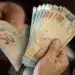 Mãos contando cédulas de R$ 50 representando o pagamento de salário no 5º dia útil de abril de 2026