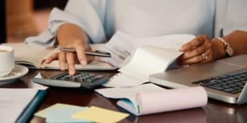 Pessoa calculando dívidas com documentos e laptop sobre a mesa, representando renegociação no Feirão Limpa Nome Serasa.