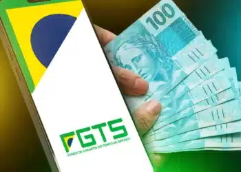 Celular com logo do FGTS e notas de R$ 100 na mão ilustrando saque-aniversário para nascidos em março.