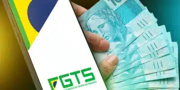 Celular com logo do FGTS e notas de R$ 100 na mão ilustrando saque-aniversário para nascidos em março.