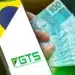Celular com logo do FGTS e notas de R$ 100 na mão ilustrando saque-aniversário para nascidos em março.