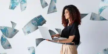 Mão segurando um leque de notas de 100 reais sobre um fundo azul vibrante com notas flutuando.