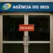 Agência do INSS fechada com placa vermelha na porta de vidro.
