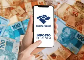 Mão segurando smartphone com logo da Receita Federal e texto Imposto de Renda sobre cédulas de real.
