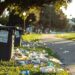 Lixeira transbordando com resíduos plásticos espalhados em parque.